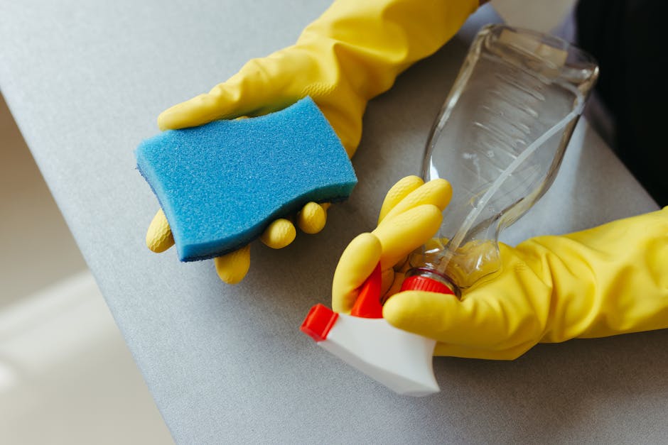 A woman with curly hair is performing domestic cleaning in a modern living room, using a mop on the smooth, light grey tiled floor. She is dressed in casual, comfortable clothing and appears to be cle