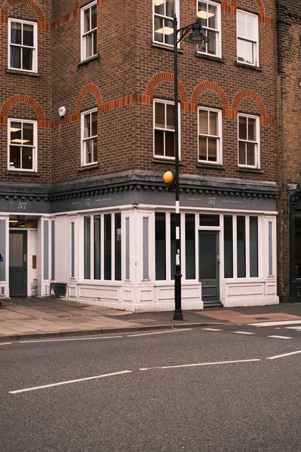 Exterior view of a three-story brick building with white wooden window frames and a ground-floor storefront painted in white, featuring large glass windows and a door. The sidewalk in front is clean, 